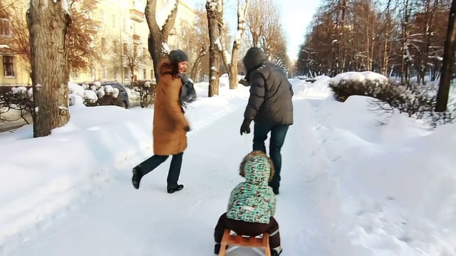 一家人正用雪橇拉儿子沿路而行。视频素材