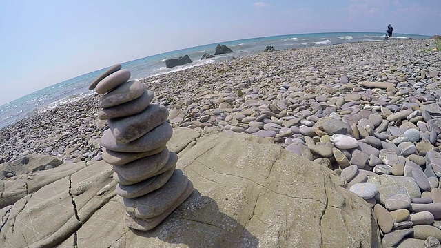 在空旷的野生海滩上的鹅卵石金字塔男性旅行者沿着冲浪推自行车视频素材