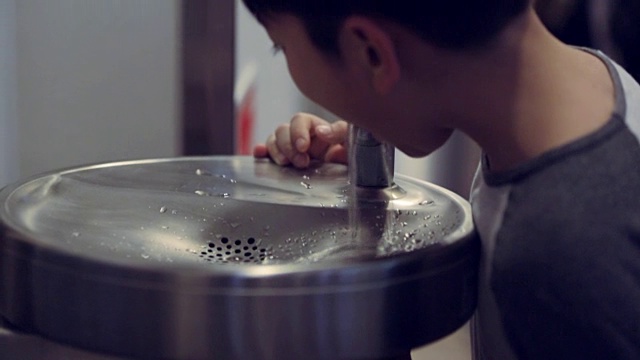 亚洲男孩在室内饮水机旁喝水视频素材