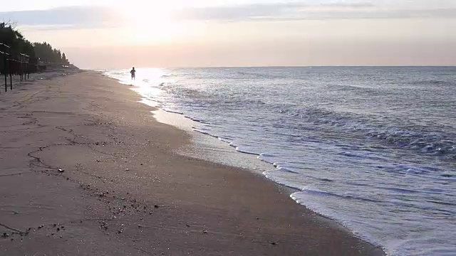 日出日落时在海滩上慢跑的人。视频素材