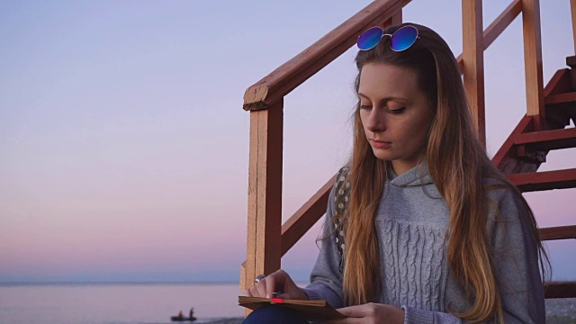 旅游:美丽的女孩游客在海滩上画日落。中景，慢镜头，手持式。视频素材