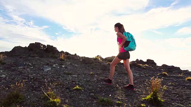 背包徒步旅行者在一个有太阳耀斑的山顶徒步旅行。年轻健康女性在大自然中冒险。视频素材