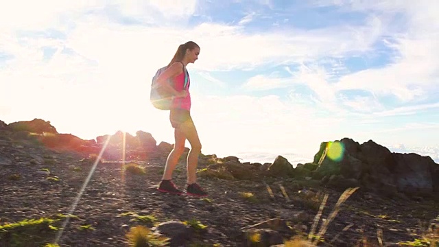 背包徒步旅行者在一个有太阳耀斑的山顶徒步旅行。年轻健康女性在大自然中冒险。视频素材