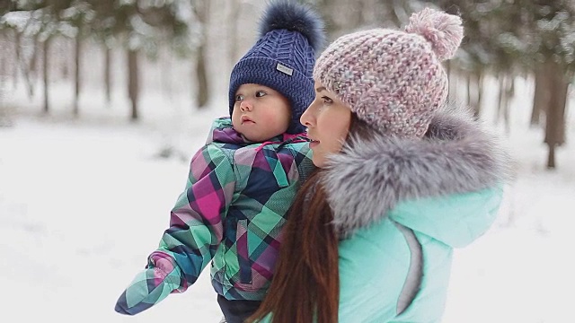 快乐的妈妈抱着宝贝女儿在冬日雪地里散步视频素材