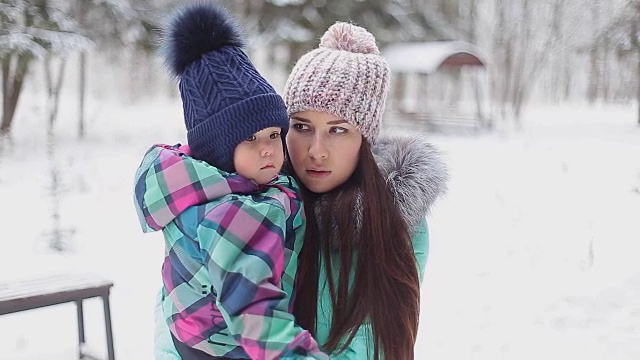 快乐的妈妈抱着宝贝女儿在冬日雪地里散步视频素材