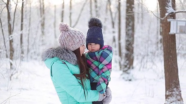 快乐的妈妈抱着宝贝女儿在冬日雪地里散步视频素材