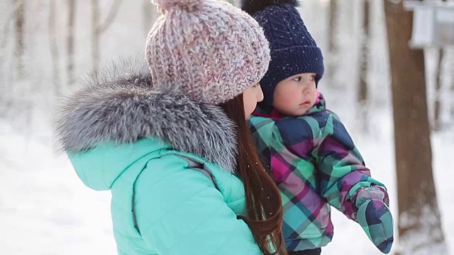 快乐的妈妈抱着宝贝女儿在冬日雪地里散步视频素材