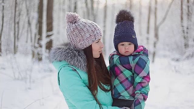 快乐的妈妈抱着宝贝女儿在冬日雪地里散步视频素材