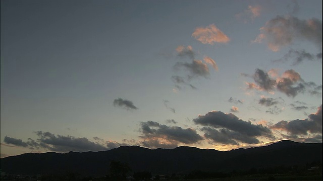 在夕阳的照耀下，乌云在蓝天上缓缓飘过，山上的剪影视频素材