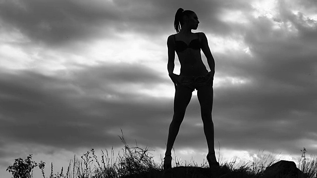 身材苗条的女孩拍照模特在一个多云的天空为背景拍摄的田野上，黑白视频中，一个女人的剪影视频素材