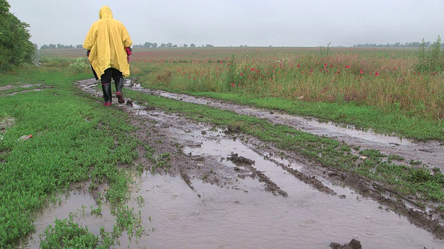 人们在雨中走在泥泞的路上穿过田野视频素材