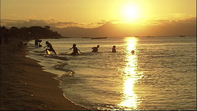 夕阳西下时，孩子们在浅水中嬉戏和游泳的剪影视频素材