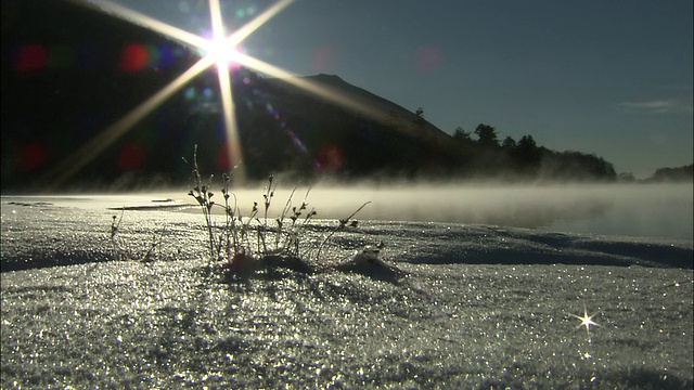 薄雾漂浮在湖面上，太阳照射在山的轮廓上，前景是白雪皑皑的海岸视频素材