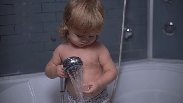 4K卷毛可爱小男孩在浴缸里洗澡，把水倒在手臂上，微笑着对着镜头挥手视频素材