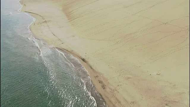 海浪冲上鸟取沙丘下面的海滩。空中拍摄视频素材