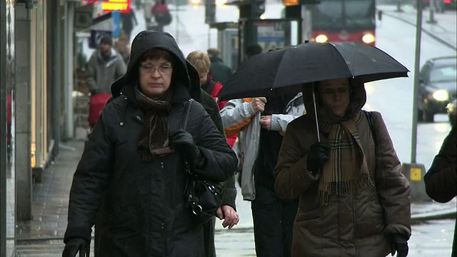 行人在雨中行走时穿有帽外套或带伞。视频素材