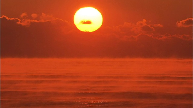 当炽热的太阳在地平线上发光时，海雾漂浮在橙色的海面上。视频素材