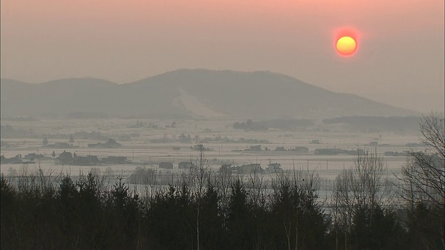 清晨的阳光穿过朦胧的天空，越过高山和白雪覆盖的农田。视频素材