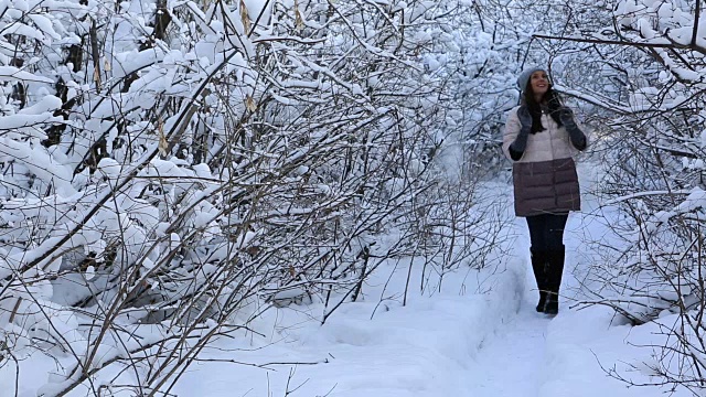 美丽快乐的女孩在冬天的公园散步，欣赏白雪覆盖的树枝视频素材