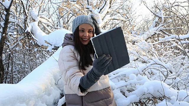 漂亮快乐的女孩在平板电脑上用Skype聊天。冰雪覆盖的树木在冬季公园视频素材