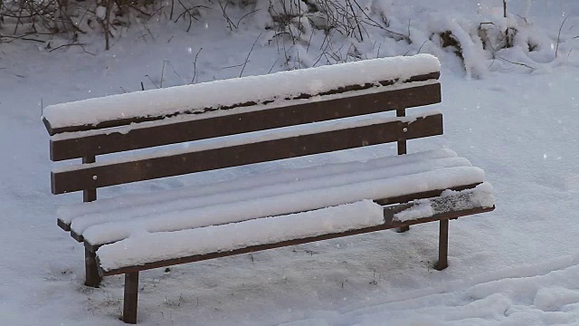 寒冷的冬日里飘着小雪，公园里白雪覆盖着空荡荡的长凳。视频素材