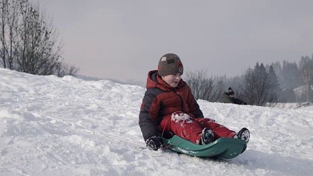 小男孩从山上的雪橇上爬下来视频素材