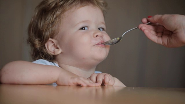 可爱的小婴儿在餐桌上用勺子喂奶，小男孩吃着固体食物视频下载