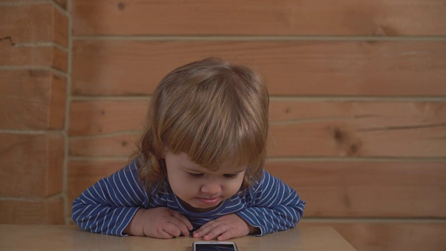 漂亮的小婴儿在木屋里看着手机微笑着视频下载