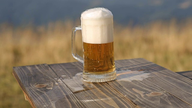 桌上放着一杯新鲜啤酒，背景是麦田和群山视频素材