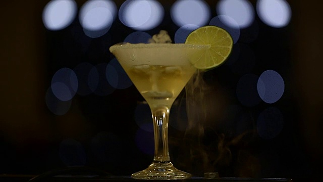 黄色酒精鸡尾酒，装在马提尼玻璃杯中，黑色背景上加一片酸橙视频下载