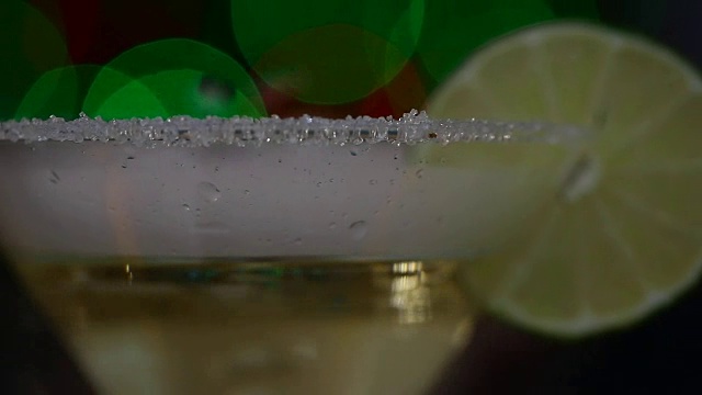 白色的雾霾在一个酒精饮料的杯子上，黑色的背景与绿色和蓝色的散焦视频素材
