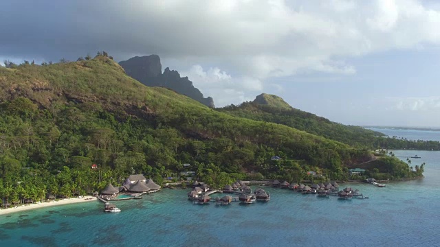 AERIAL:豪华的海滩度假胜地，有豪华的水上别墅和梦幻般的海滨别墅，在美丽的蓝绿色泻湖上，在异国情调的岛屿博拉博拉，背景是著名的山脉地标视频素材