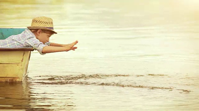 戴着草帽的男孩坐在船上，从木板上洒水视频素材