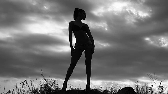 身材苗条的女孩拍照模特在一个多云的天空为背景拍摄的田野上，黑白视频中，一个女人的剪影视频下载