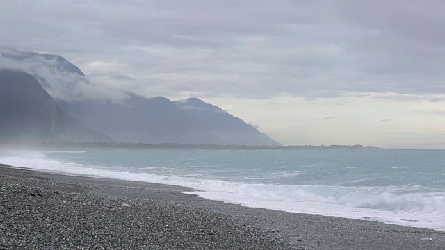 强烈的海浪冲刷着以山为背景的卵石滩。视频素材