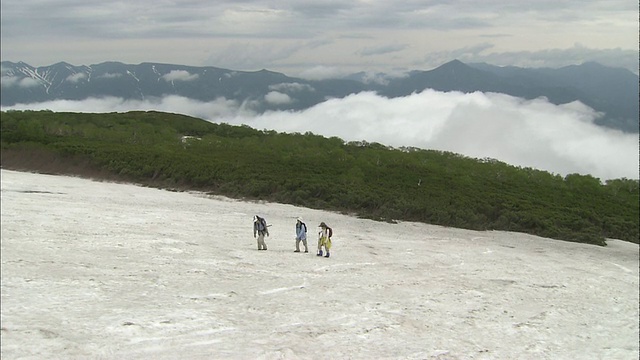 镜头从山谷里的云雾中缩小到北海道大泽山(Mount Taisetsu)上的三位登山者视频素材