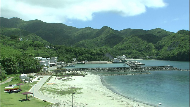 郁郁葱葱的青山环绕着日本小笠原岛附近的海滩和港口。视频素材