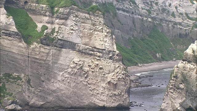 一颗巨石躺在千球角陡峭悬崖下的海滩上。视频素材