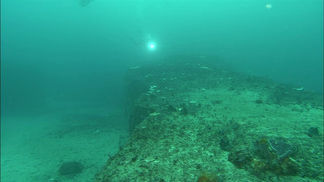 在日本静冈县大崎市附近的海底，一名潜水员正穿过巨大的巨石。Diving-shot视频素材