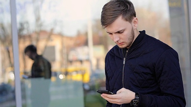 英俊严肃的男人在街上用智能手机发短信。视频素材