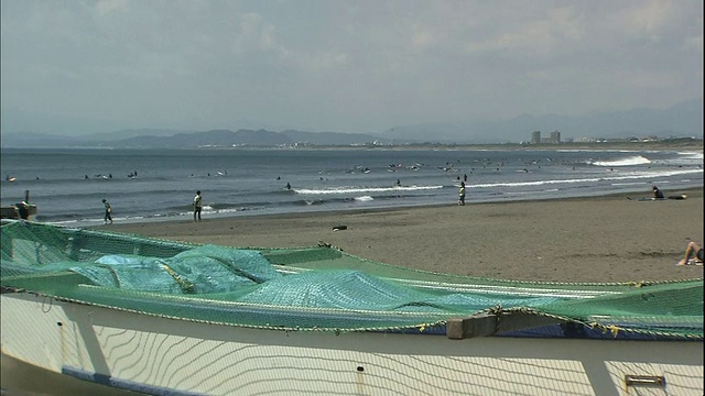 冲浪者在海岸附近的浪尖上冲浪，在湘南海滩上的渔船上冲浪。视频素材