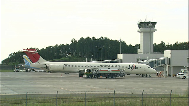 日本富士山静冈山机场，一架日本航空公司的喷气式飞机在空中交通管制塔附近的停机坪上伸展。视频素材