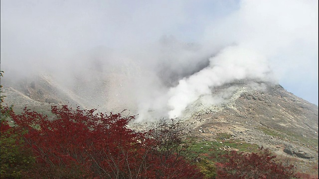 在覆盖山坡的秋叶附近，Nasudake火山升起了缕缕烟雾。视频素材