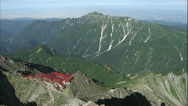 几缕白云笼罩在日本南部的阿尔卑斯山脉上，在那里，雅力加三索(Yarigatake Sanso)山间小屋坐落在郁郁葱葱的山坡之间。视频素材