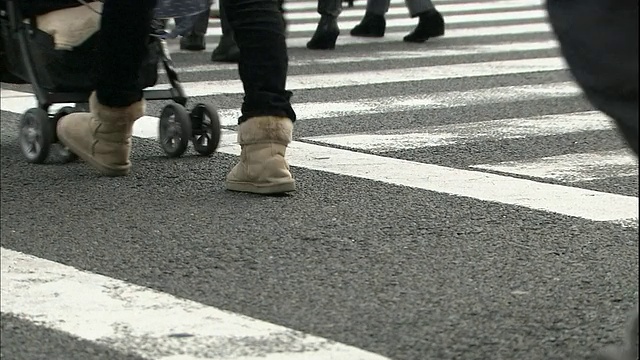 穿着制服的学生与行人一起走在城市街道的人行横道上。视频素材