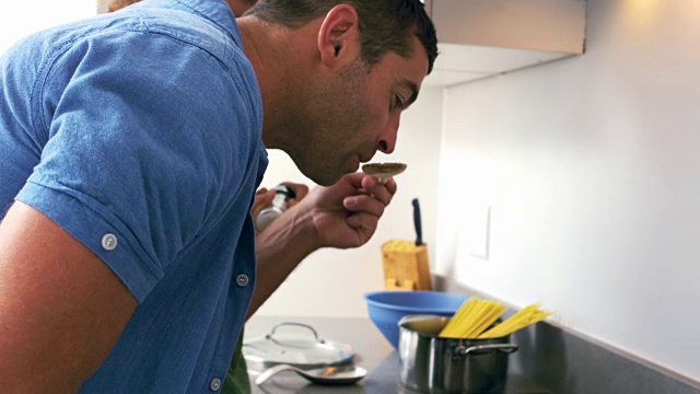 可爱的夫妇在厨房做饭和男人品尝酱汁视频素材