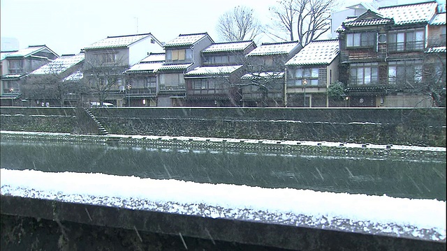 在Kazue-machi茶屋区，积雪堆积在河岸和传统木屋的屋顶上。视频素材