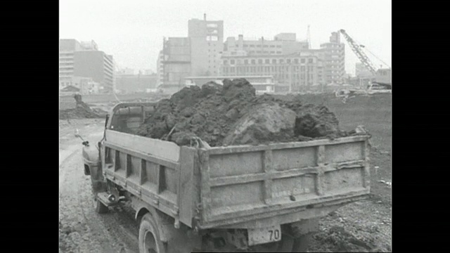 一辆挖土机装满了一辆自卸卡车，沿着东京的友桥净化厂(Yodobashi Purification Plant)的工地行进。视频素材