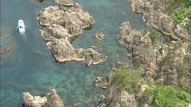 一艘游船驶过日本佐渡岛海岸崎岖的岩层。视频素材