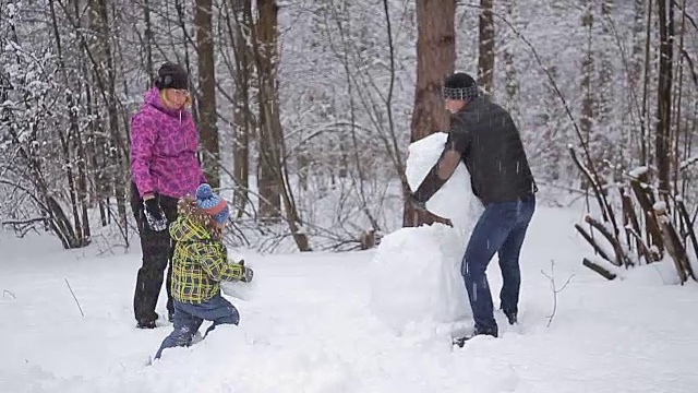 快乐的小家庭在清新的雪中玩耍，在美丽阳光明媚的冬日户外堆雪人视频素材